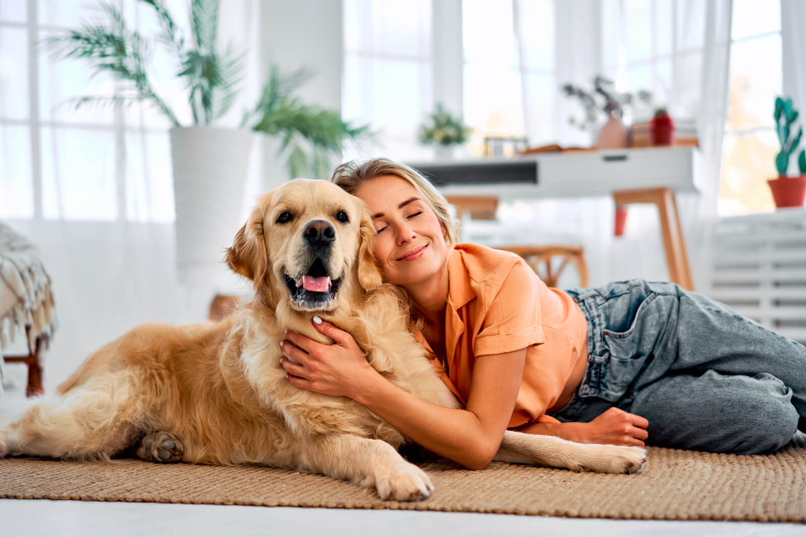 Woman lying on the floor with a golden retriever in a bright living room.